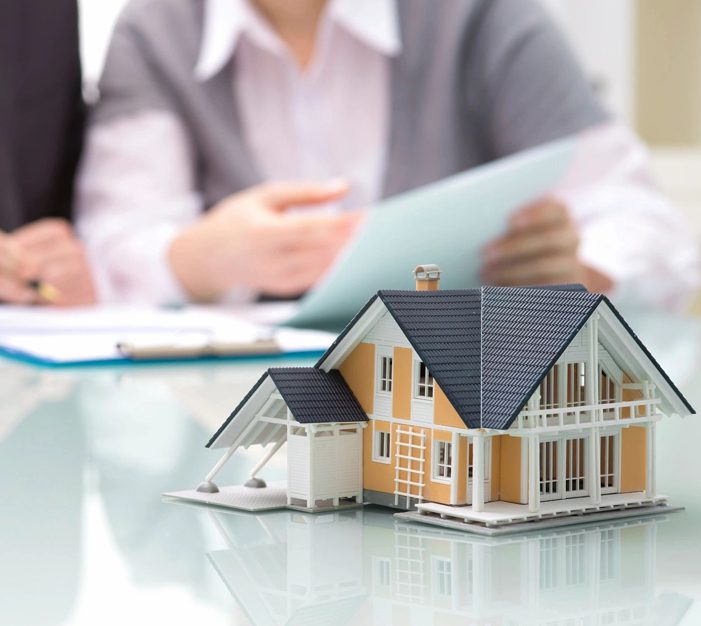 A person sitting at a table with papers and a model house.